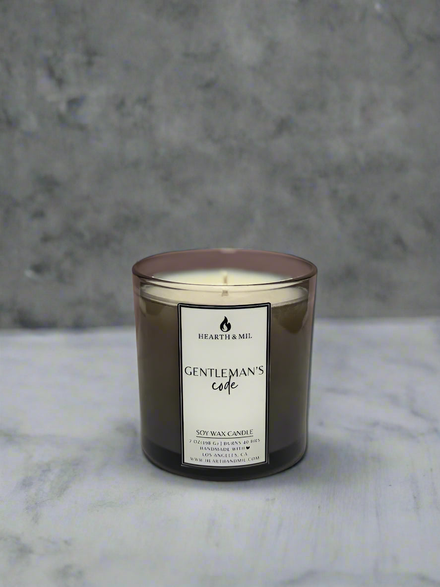 Black candle labeled 'Gentleman's Cade' on a white surface with a pink background